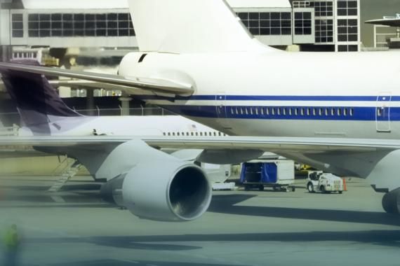 A stock image of an airport apron with two airplanes in the foreground and an airport building in the background