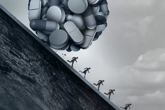 A black-and-white graphic depicts a large ball of pills rolling down a hill while human figures run away from it.