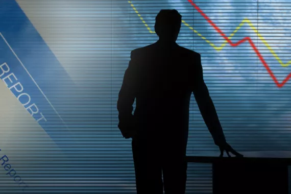 A silhouette of a man stands at a desk and looks into the distance. In the background are graphics representing the world of finance.