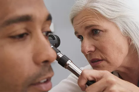 A female doctor examines a male patient's left ear with an otoscope.