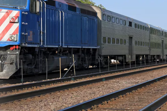 A blue locomotive stands on railroad tracks with grey railcars behind it