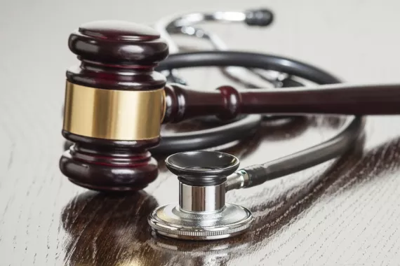 A judge's gavel and a doctor's stethoscope rest side-by-side on a table