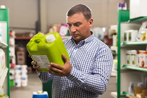 A man in a hardware store reads the label of a green plastic container