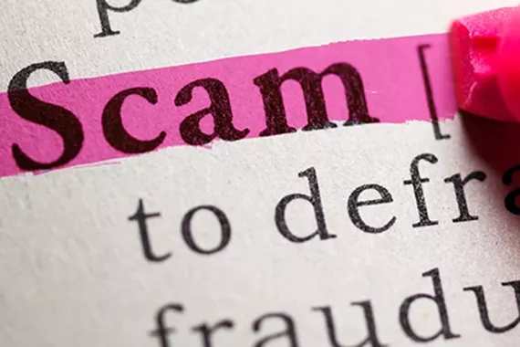 Close-up of a white page with a few words printed in black ink. The word “Scam” at the top of the page is bolded and highlighted in pink