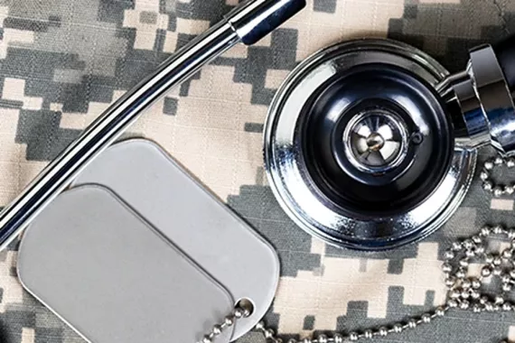 Military dog tags and a physician’s stethoscope displayed on camouflage uniform fabric