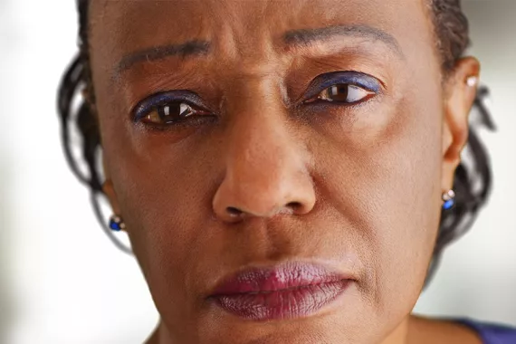 A close-up view of a Black woman facing a camera. Her expression is serious and worried.