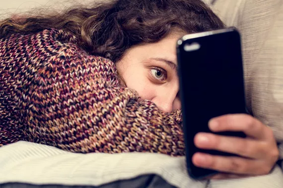 A young girl lying on her stomach looks at her phone.