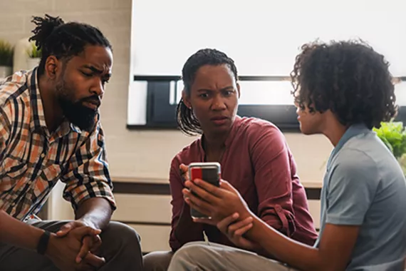 A boy shows a man and a woman his phone. The adults have concerned expressions on their faces.