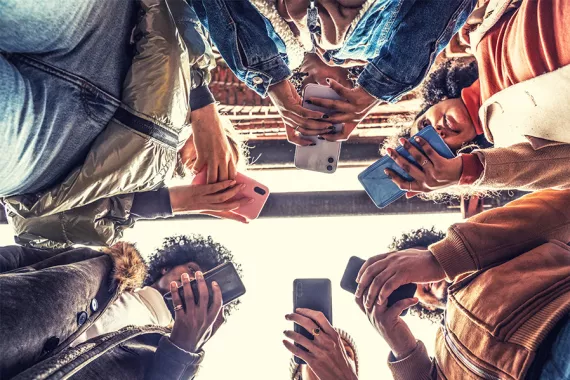 Photographed from below, six people stand in a circle looking at their phones.