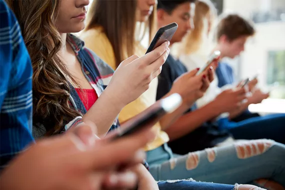 Young people sit in a row and look at their phones.