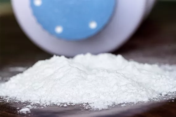 A pile of white talcum powder lies on a flat surface with a baby powder-like container in the background.