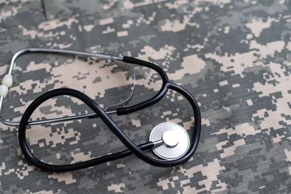 A physician’s stethoscope is placed on camouflage print fabric.