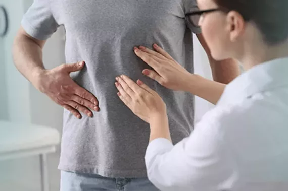 A doctor wearing a white coat feels the abdomen of a men who is also touching his abdomen