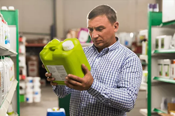 A man in a hardware store reads the label of a green plastic container