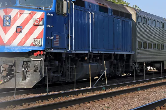 A blue locomotive stands on railroad tracks with grey railcars behind it