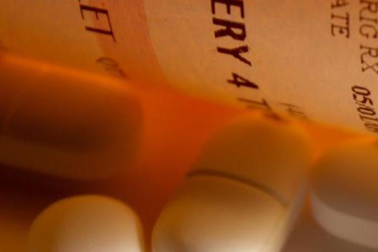 A partial picture of a prescription bottle and a few loose pills.